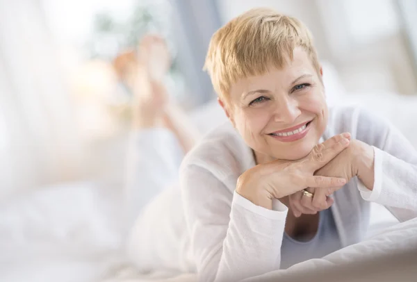 Felice donna riposo mento su mani mentre sdraiato a letto — Foto Stock