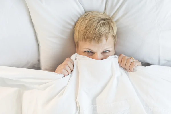 Mujer mirando a través de edredón en la cama — Foto de Stock