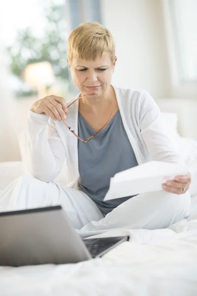 Woman Reading Document With Laptop On Bed — Stock Photo, Image