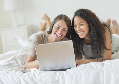 Happy Female Friends Using Laptop In Bed clipart