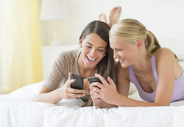 Друзья, которые используют смарт-телефоны, пока лежат в постели — стоковое фото