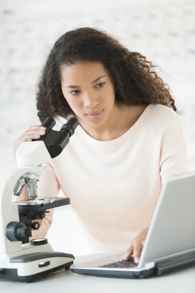 Chica usando el ordenador portátil y microscopio en la clase de química —  Fotos de Stock