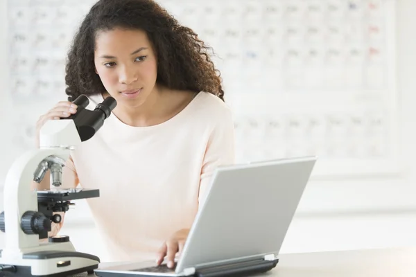 Девушка с ноутбуком и микроскопом в классе химии — стоковое фото