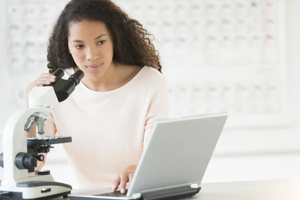 Menina usando laptop e microscópio na classe de química — Fotografia de Stock