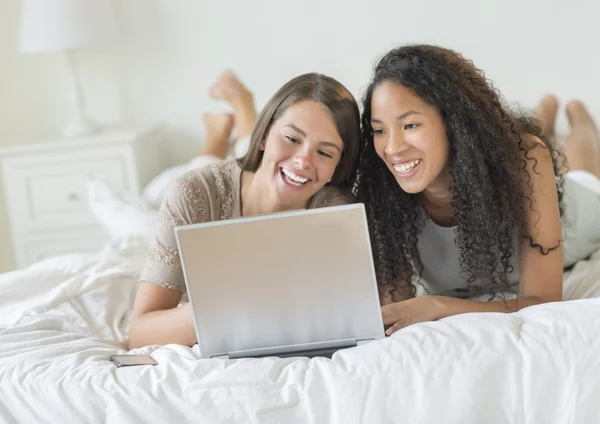 Amigos femeninos felices usando el ordenador portátil en la cama — Foto de Stock