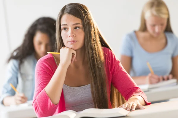 Promyšlené dospívající dívka sedí u stolu v učebně — Stock fotografie