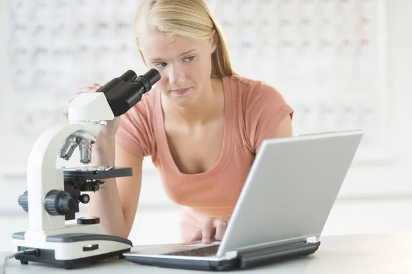 Студент дивиться ноутбук під час використання мікроскопа — стокове фото