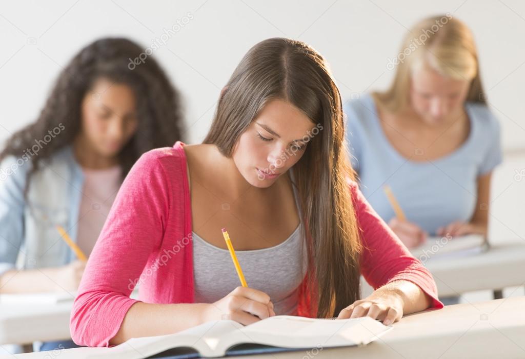 Teenage Students Writing In Book At Desk