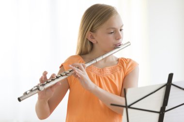 Girl Looking At Sheet Music While Practicing Flute clipart