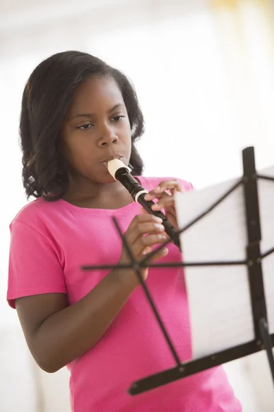 Chica con partitura tocando flauta en casa — Foto de Stock