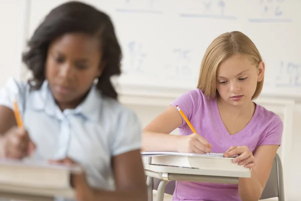 Schoolmeisjes schrijven van notities op Bureau — Stockfoto