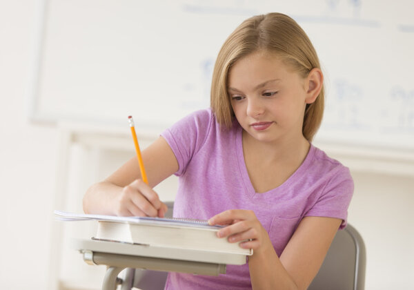 Schoolgirl Writing Notes In Book At Classroom