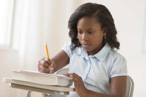 Colegiala escribiendo notas en el bloc de notas en el escritorio — Foto de Stock