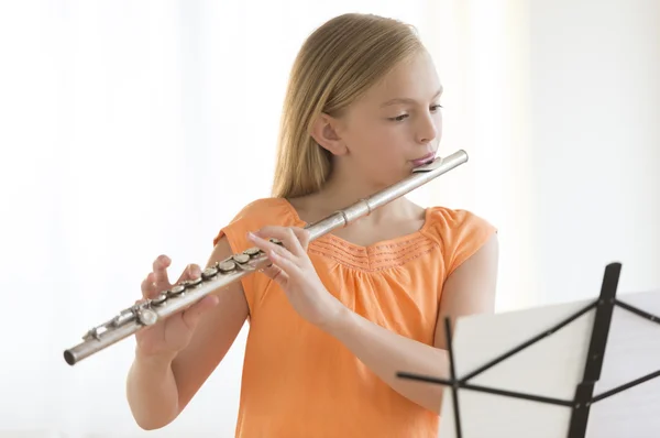 Dívka při procvičování flétna při pohledu na noty Royalty Free Stock Fotografie