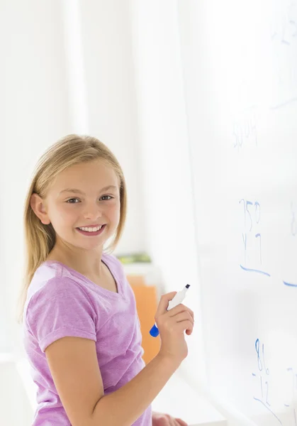 Fille heureuse avec stylo debout près du tableau blanc en salle de classe Image En Vente
