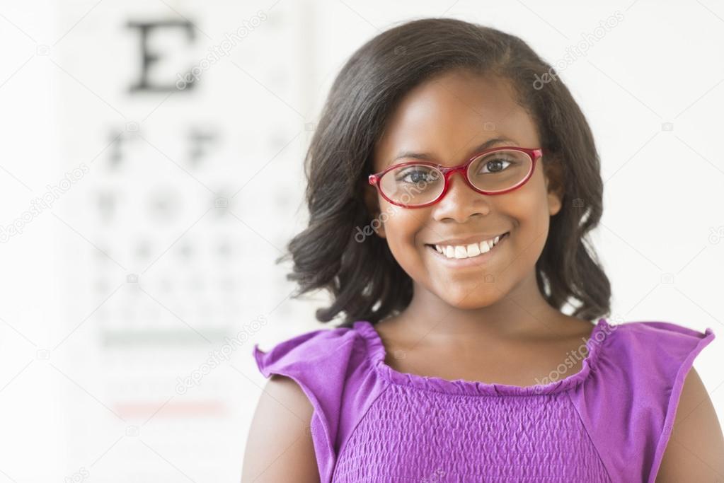 Girl Wearing Glasses Against Eye Chart In Clinic
