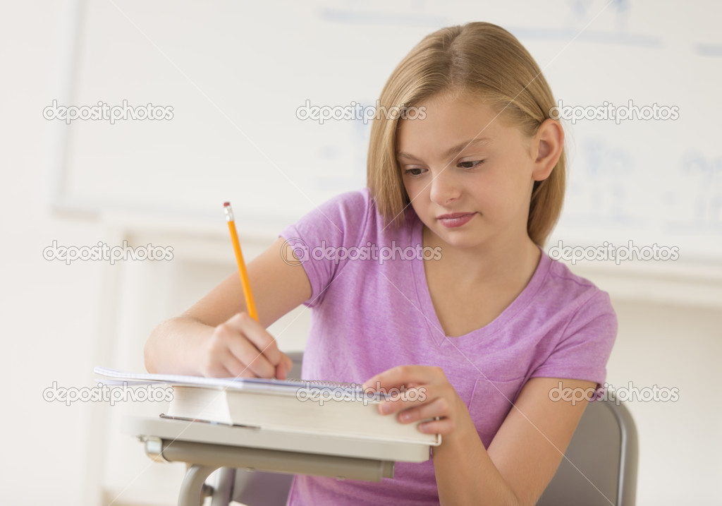 Schoolgirl Writing Notes In Book At Classroom