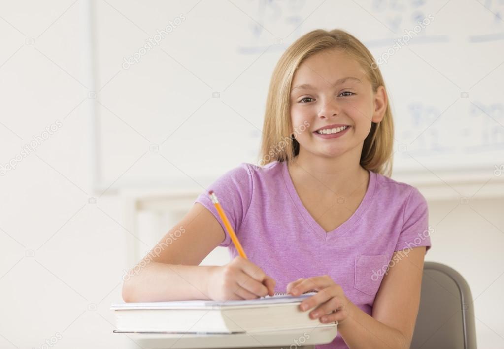 Schoolgirl Writing Notes In Book At Desk