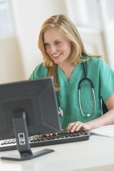 Feliz doctor en exfoliantes usando computadora en el escritorio del hospital — Foto de Stock