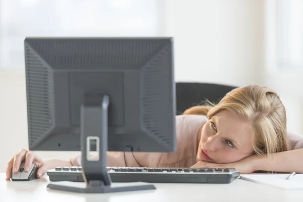 Geschäftsfrau blickt auf Desktop-PC, während sie sich auf Schreibtisch lehnt — Stockfoto