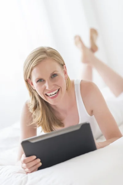 Mujer sosteniendo la tableta digital mientras está acostado en la cama — Foto de Stock
