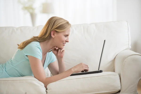 Mulher usando laptop enquanto deitado no sofá — Fotografia de Stock