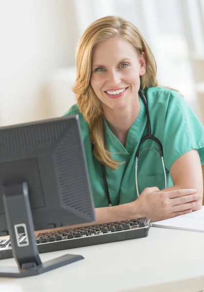 Vertrouwen vrouwelijke arts in scrubs leunend op ziekenhuis Bureau — Stockfoto