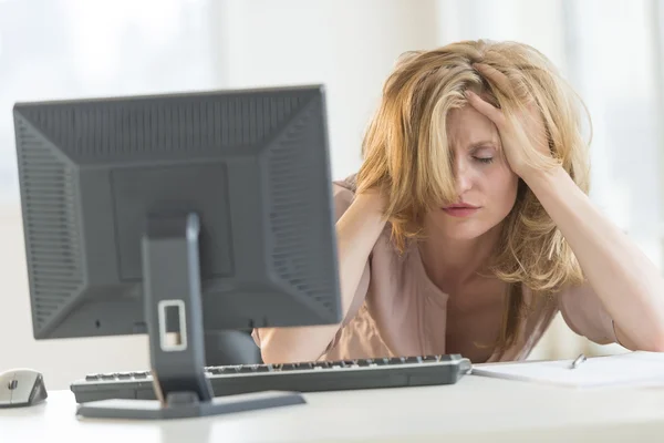 Frustrierte Geschäftsfrau mit Händen im Haar sitzt am Schreibtisch — Stockfoto