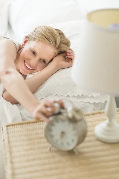 Mujer alcanzando el reloj despertador mientras se acuesta en la cama Imagen de archivo