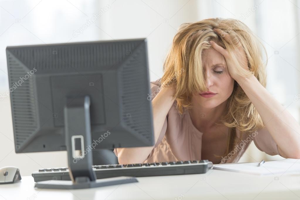 Frustrated Businesswoman With Hands In Hair Sitting At Desk