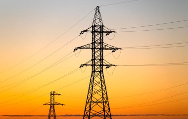 Yüksek voltaj kuleleri ve elektrik hatları sarı gündoğumu gökyüzüne karşı.