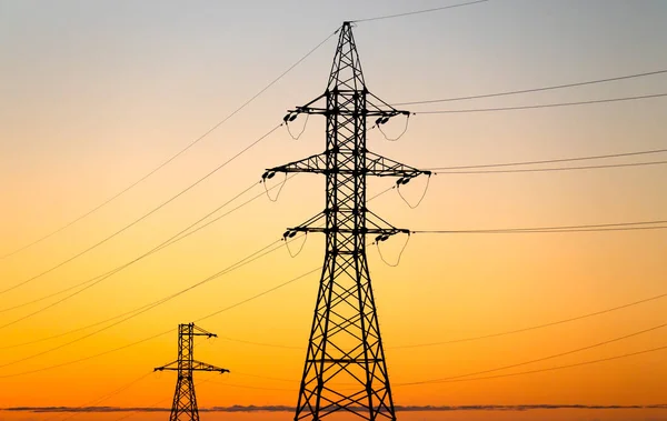 Yüksek voltaj kuleleri ve elektrik hatları sarı gündoğumu gökyüzüne karşı.