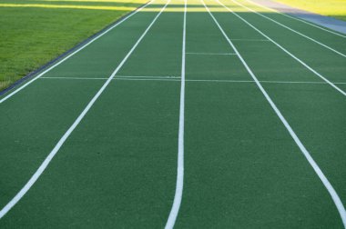 Green color rubber running track in nature at bright summer day.