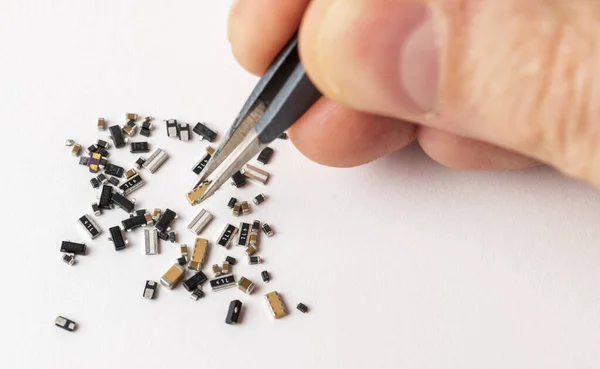 Human hand with tweezers over the various micro electronic elements on white background.