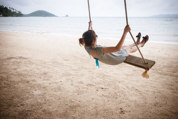 Happy asian girl on a swing on a beach