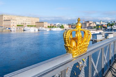 Golden Crown of Skeppsholmen Bridge, Swedish: Skeppsholmsbron, with blue sea and historical buildings of Stockholm on background, Sweden clipart