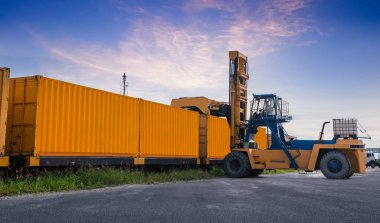 Forklift kamyonu bir tren istasyonunda kargo konteynırlarını kaldırıyor, dağıtım terminali mallarının yüklenmesini bekleyen demiryolu ithalat ve ihracat lojistik taşımacılık konsepti..