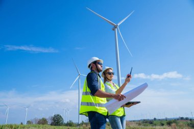 Üniforma giyen mühendis, kask teftişi ve rüzgar güneş pili panelinde elektrik enerjisi üretmek için araştırma yapıyor. Yeşil ekolojik enerji üretimi rüzgar sürdürülebilir enerji kavramı.