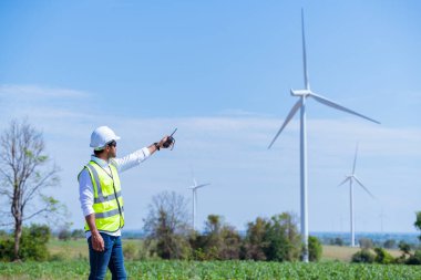 Üniforma giyen mühendis, kask teftişi ve rüzgar güneş pili panelinde elektrik enerjisi üretmek için araştırma yapıyor. Yeşil ekolojik enerji üretimi rüzgar sürdürülebilir enerji kavramı.