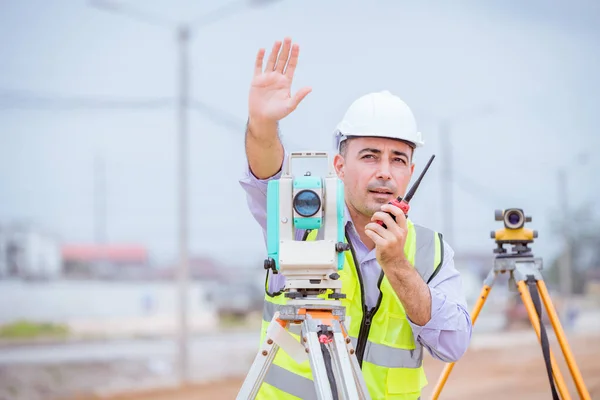 Surveyor engineers wearing safety uniform ,helmet and radio communication with equipment theodolite to measurement positioning on the construction site of the road with construct machinery background.