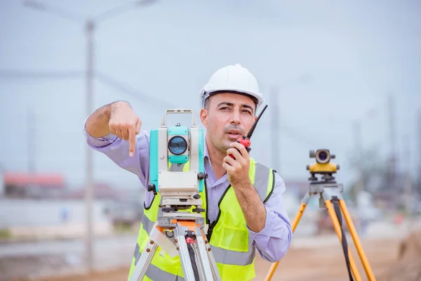 Surveyor engineers wearing safety uniform ,helmet and radio communication with equipment theodolite to measurement positioning on the construction site of the road with construct machinery background.