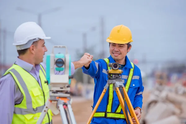 Surveyor engineers wearing safety uniform ,helmet and radio communication with equipment theodolite to measurement positioning on the construction site of the road with construct machinery background.