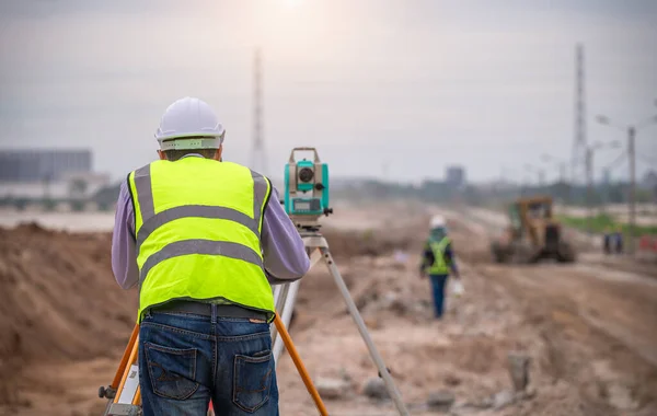 Surveyor engineers wearing safety uniform ,helmet and radio communication with equipment theodolite to measurement positioning on the construction site of the road with construct machinery background.