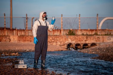 Çalışan su analizi ve su kalitesi altında koruyucu üniforma ve eldiven giyen bilim adamları laboratuvardaki vakayı kontrol etmek için atık su getirerek çevre kirliliği sorunu kavramı