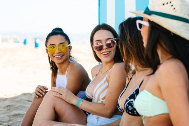 Four young women in bikinis talking to each other leaning against the beach wall