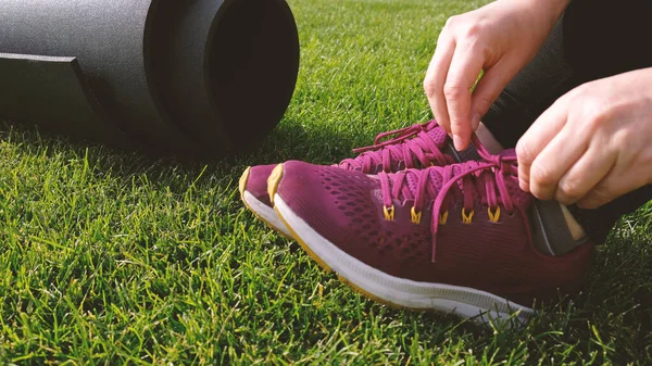 Genç kadın pembe ayakkabının bağcıklarını bağlıyor. Kadın, arka bahçedeki yeşil çimlerde ya da parkta yoga ya da spor yapmaya hazırlanıyor. Koşmadan önce ısın. Sağlıklı yaşam tarzı.