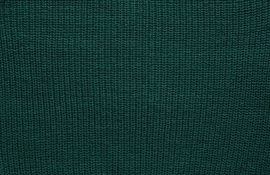Düz örülmüş koyu yeşil süveter desenli. Üst manzara, yakın plan. El yapımı yün ya da pamuk kumaş dokusu. Büyük kaburgaların arka planı örgü iğneleri ya da örgü örgüleriyle örülmüş..