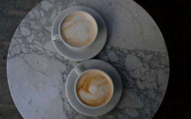 Kahve dükkanında mermer masa zemininde köpükle süslenmiş iki bardak kapuçino ya da latte. Birbirine aşık çiftler için sabah kahvesi. Üst Manzara. İki bardak beyaz kahve..