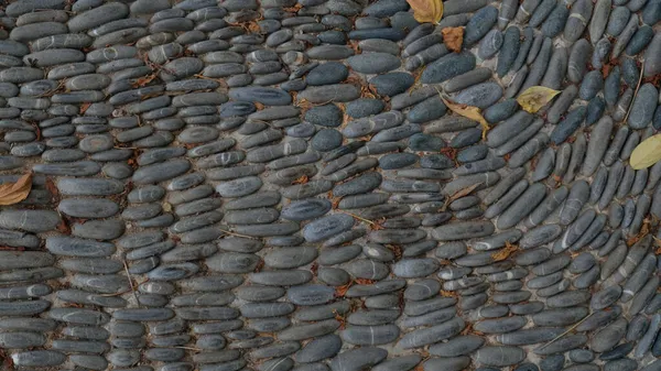 Gehweg oder Fußweg im Park aus grauem Stein, der mit abgefallenem Laub bedeckt ist. Kopfsteinpflaster Straße in der Straße. Konvexe strukturierte Steine Hintergrund. — Stockfoto