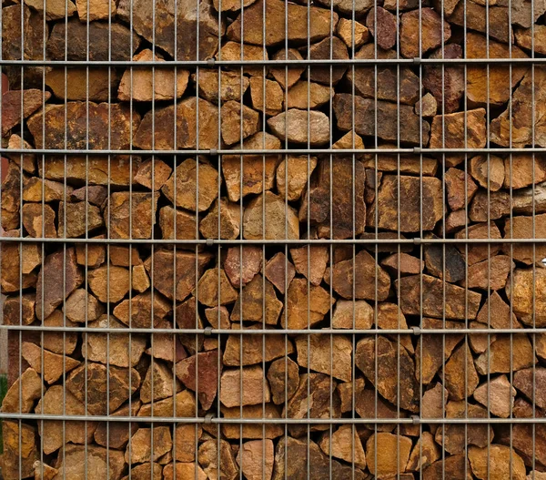 Gabion retaining wall - close-up brown stones in gabion metallic baskets kept by retaining wall. Gabions protective wall filled with stones and tied with thick metal wire. Eco wall textured design.